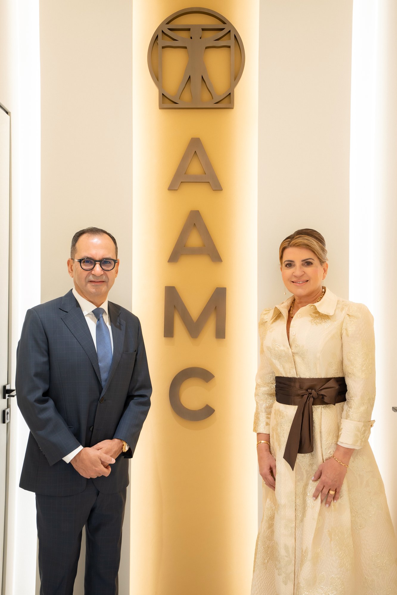Two people standing beside the AAMC wall signage inside the clinic.