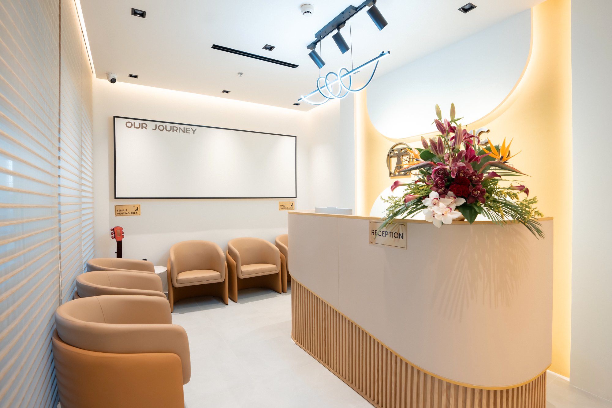 Waiting area at AAMC Polyclinic with cushioned armchairs, warm lighting and the reception desk.