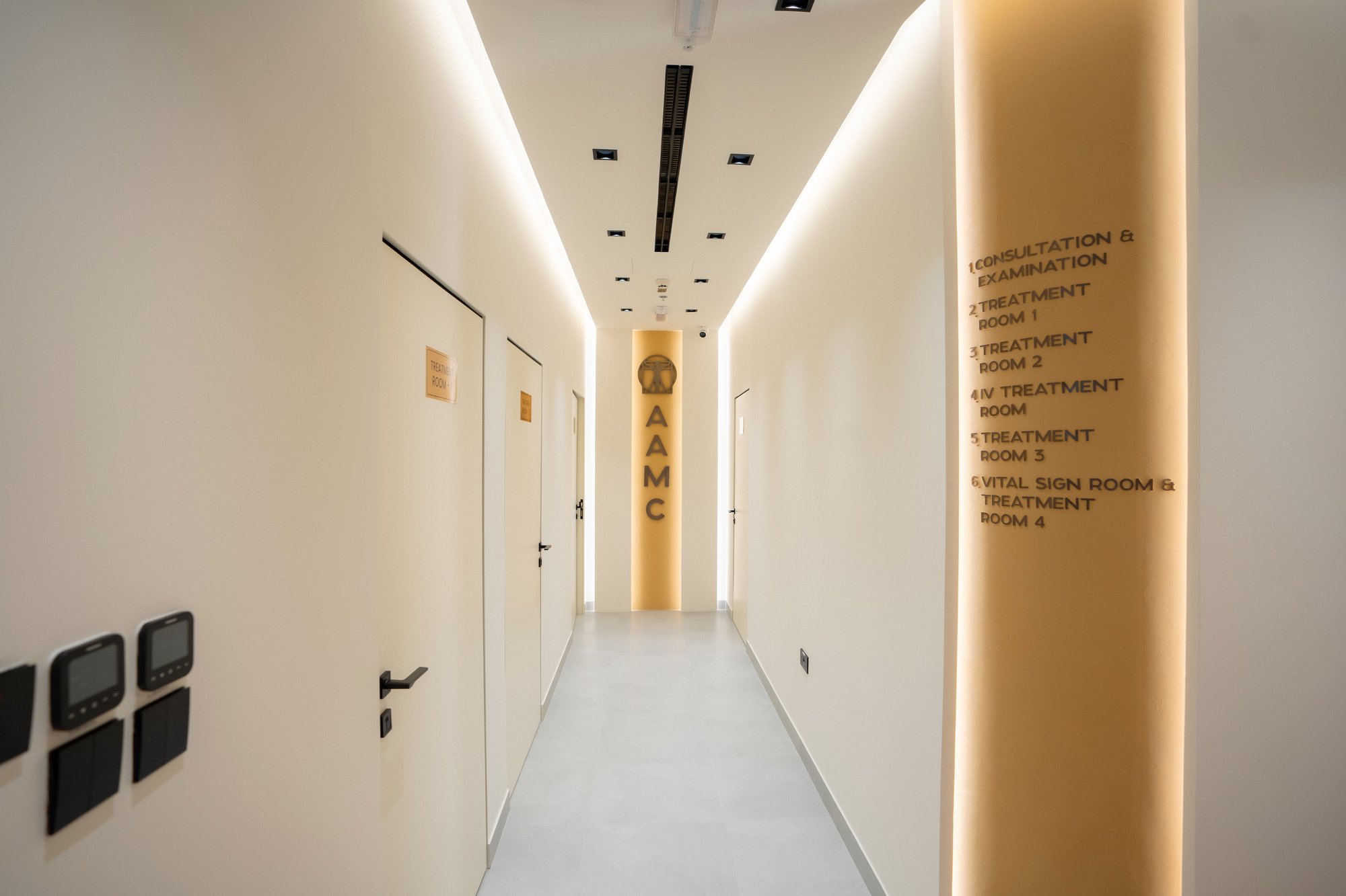 Softly lit clinic corridor at AAMC Polyclinic with signposted consultation and treatment rooms.